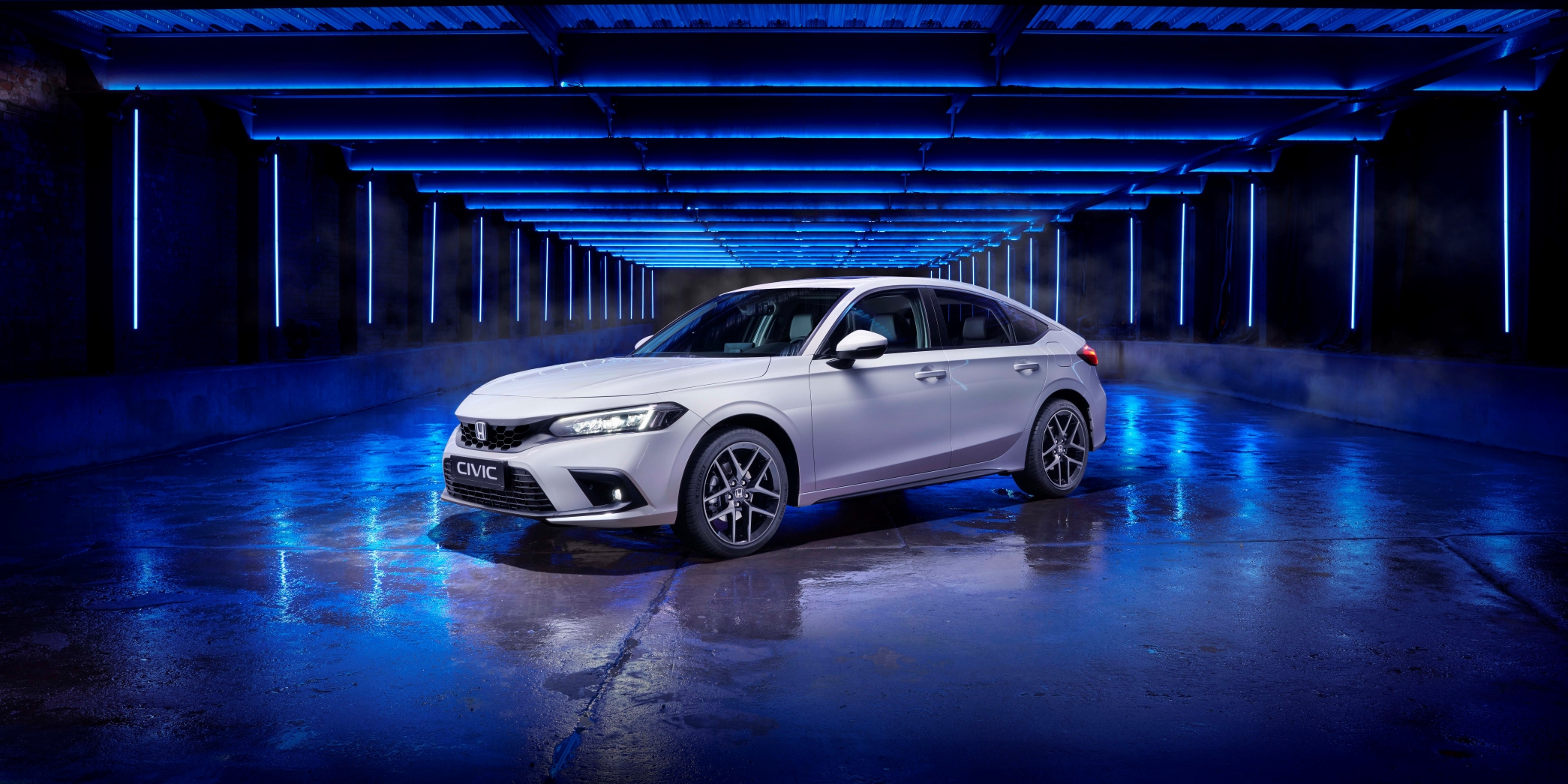 Egy új, 2022-es Honda Civic elülső háromnegyedes nézete, fehér színben, kék fénnyel megvilágított stúdióban